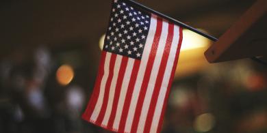 Small American flag indoors, softly lit background.