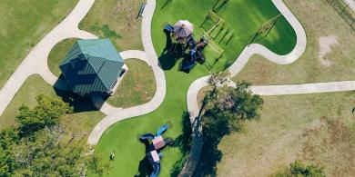 Aerial view of a playground with slides, paths, and a green-roofed pavilion.
