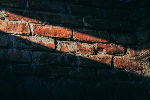 Sunlight casting shadows on a weathered brick wall.
