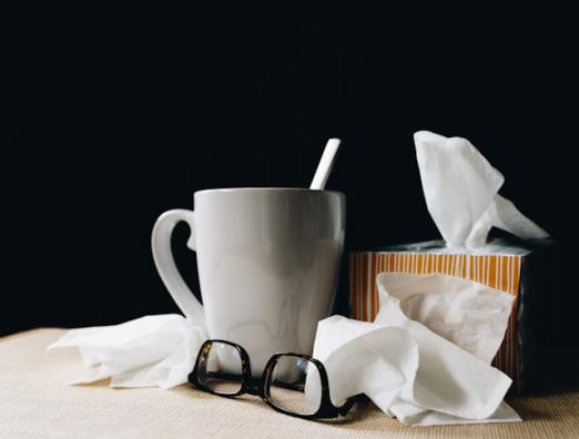 Mug with straw, tissues, and glasses on a table against a black background.