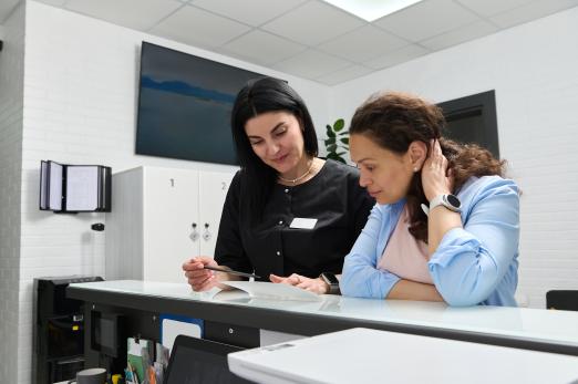 Two women discussing documents at a reception desk.
