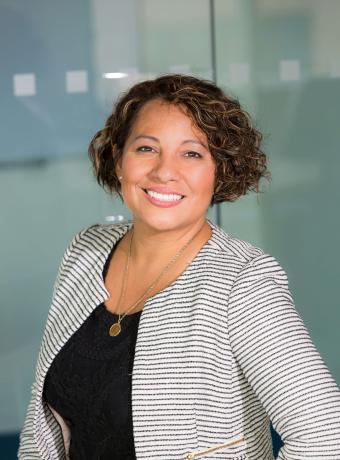 Smiling woman in office attire standing in a bright room.